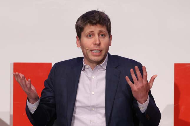 Sam Altman shrugging while speaking with his hands up, he's sitting in front of a white wall with orange panels