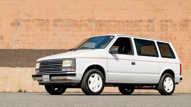 A front 3/4 shot of the white Plymouth Voyager SE parked in front of a brick wall 