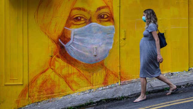 A pregnant woman wearing a face mask walks past a street mural in Hong Kong, on March 23, 2020,