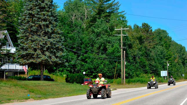 Three people ride quad bikes on a road. 