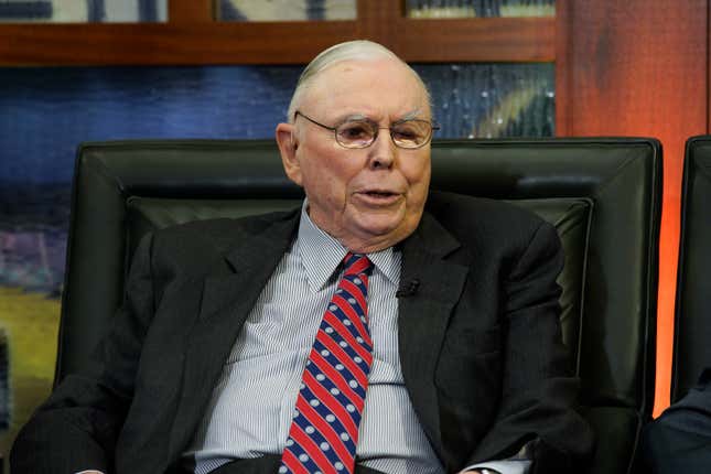 Charlie Munger sits for an interview in a suit, striped shirt, and red striped and blue polka-dotted tie