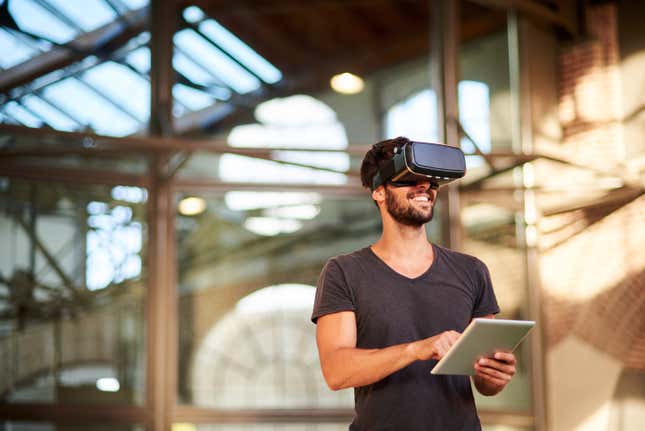 man wearing virtual reality headset, holding a touchpad, standing inside a building under construction