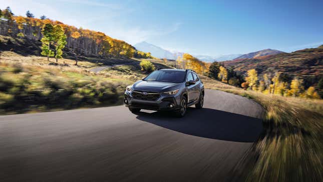 Un Crosstrek gris conduisant sur une route rurale devant des arbres et des montagnes