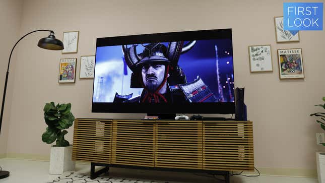 A Samsung S95D OLED TV on top of a TV stand surrounded by pictures on the wall and a PS5