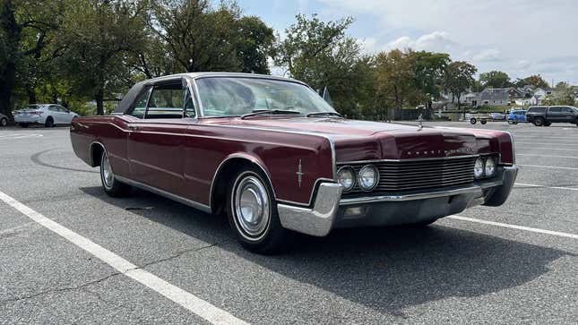 a front 3/4 shot of a 1966 maroon Lincoln COntinental coupe parked in a parking lot