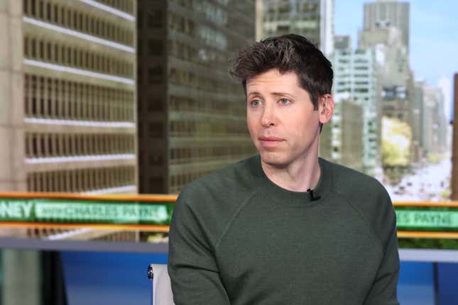 Sam Altman wearing a greenish grey sweatshirt smiling and looking out onto something