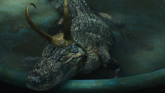 Alligator Loki reclines in a pool, looking majestic in his horns.