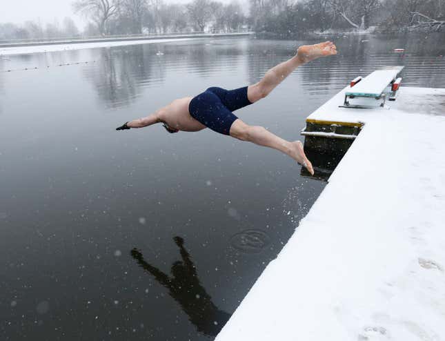 A swimmer dives into the men's pond as snow falls on Hampstead Heath