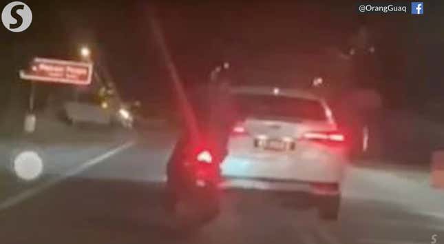 The blurry back of a Toyota Vios on a dark road in Malaysia. A motor bike follows close behind.