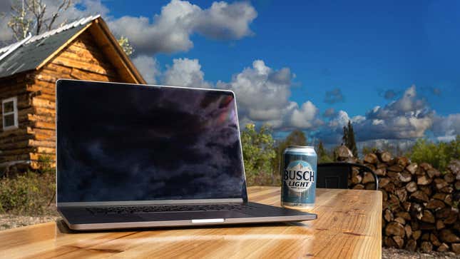 Laptop open on desk next to can of Busch Light, rustic outdoor background
