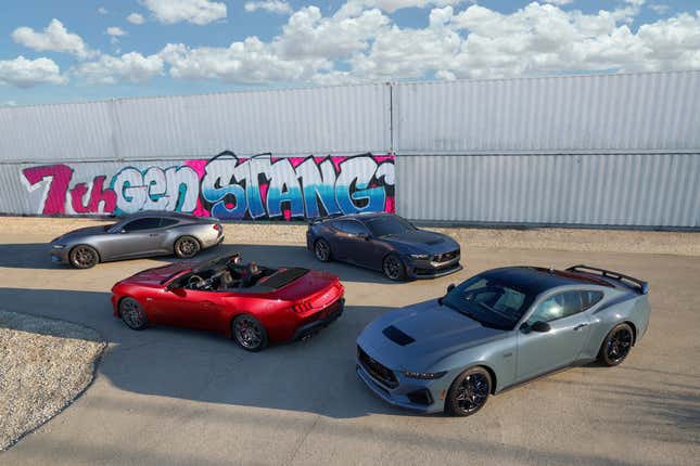 Four trim levels of 2024 Ford Mustang are parked in front of shipping containers.