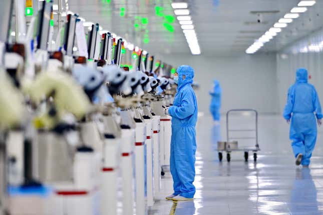 employees wearing blue hazmat suits walking while one looks at a line of machines