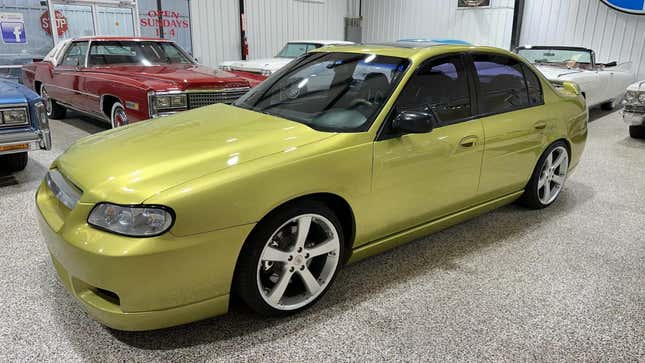 A front 3/4 view of the sublime lime Malibu parked in front of other old American cars in a garage