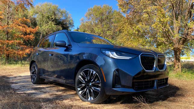 a gray bmw x3 parked on dirt in front of trees