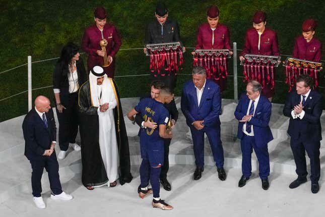 FILE - Qatar Airways staff in uniform, in background, assist in the medal ceremony, as French President Emmanuel Macron hugs France&#39;s Kylian Mbappe who was awarded the Golden Boot after the World Cup final soccer match between Argentina and France at the Lusail Stadium in Lusail, Qatar, on Dec. 18, 2022. Qatar Airways will be FIFA’s airline sponsor at the men’s 2026 World Cup being played across North America. Soccer’s governing body renewed with the company through 2030 on Wednesday, Nov. 22, 2023. (AP Photo/Thanassis Stavrakis)