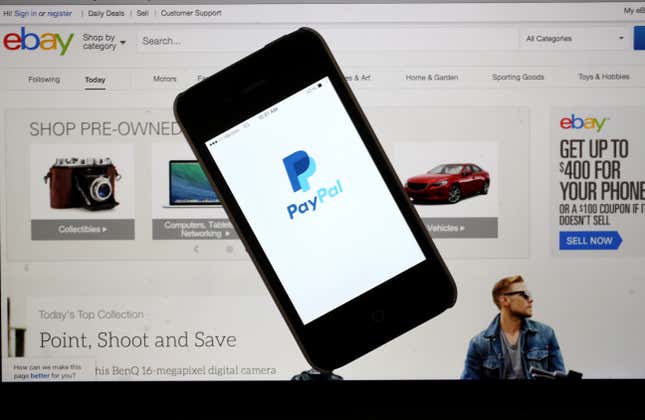 PayPal is shown on a smart phone in front of a computer screen showing an eBay window.