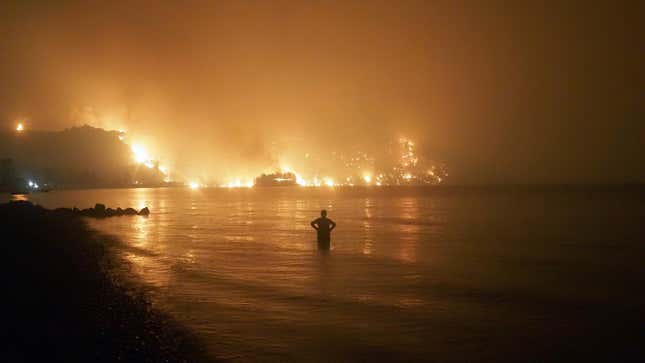 A man watches the flames as wildfire approaches Kochyli beach near Limni village on the island of Evia, late Friday, Aug. 6, 2021.