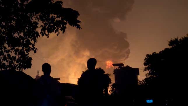 In this image made from video, residents watch a plume of smoke from a burning oil depot, in Conakry, Guinea, Monday, Dec. 18, 2023. An explosion and inferno at Guinea’s main fuel depot in the capital of Conakry has left several people dead or injured. Guinea’s presidency says the fire broke out at the Guinean Petroleum Company depot shortly after a massive explosion past midnight Sunday. (AP Photo)