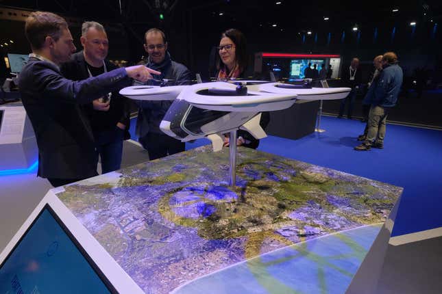 Teilnehmer inspektieren ein Modell des elektrischen Vertikalstart-und-Lande-Lufttaxis (eVTOL) des Airbus SE CityAirbus während der Amsterdam Drone Week in Amsterdam, Niederlande, am Dienstag, 27. November 2018. Die Amsterdam Drone Week, die erste offizielle europäische Plattform für Anwender, Hersteller, Dienstleister und Regulierungsbehörden, präsentiert die neueste Technologie der unbemannten Flugzeugsysteme (UAS)-Branche.