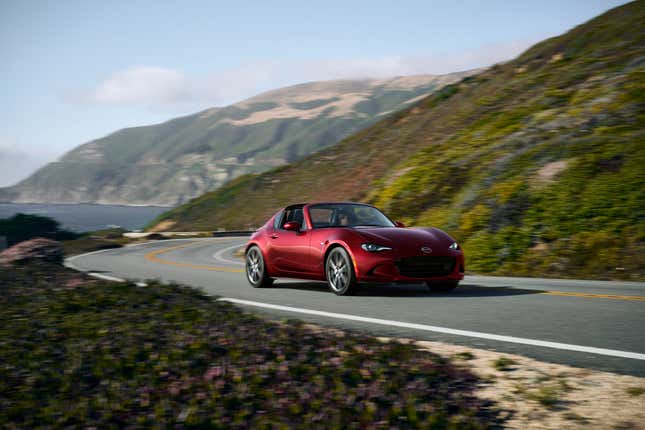 A red 2024 Mazda Miata RF driving on a coastal road with the top down