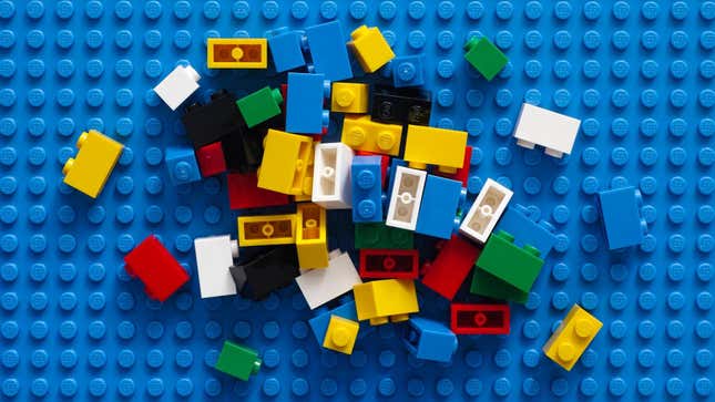 Various color Lego sit on a blue mat. 