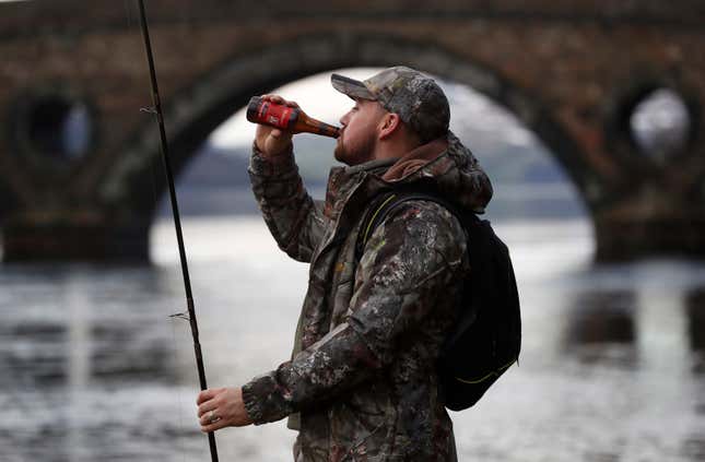 An angler drinking a beer on the opening day of salmon season on the River Tay, Scotland. 