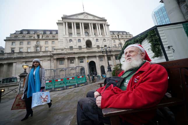 Gerard White, wearing a Santa hat and waiting for his wife to finish work, sits outside the Bank of England, which is expected to hold interest rates for the third time in a row, as fresh data has pointed towards potential cracks in the economy, in London, Thursday Dec. 14, 2023. (Yui Mok/PA via AP)