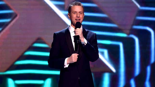 Host Geoff Keighley stands with a microsoft in his left hand during a presentation The Game Awards 2018.