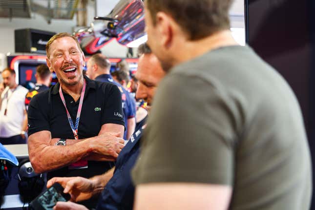 Larry Ellison (L) is laughing with his arms crossed, Horner is showing Musk something on his phone, while Musk's back is turned against the camera and is blurry