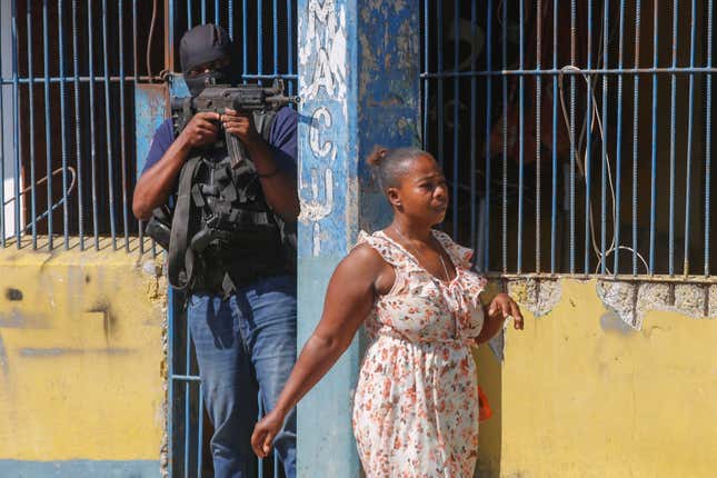 A resident walks past a National Police officer guarding the empty National Penitentiary after a small fire inside the jail in downtown Port-au-Prince, Haiti, Haiti, Thursday, March 14, 2024. This is the same prison that armed gangs stormed late March 2 and hundreds of inmates escaped. (AP Photo/Odelyn Joseph)