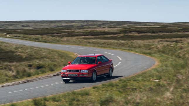 A bright red Audi S2 coupe driving around a grass-lined corner