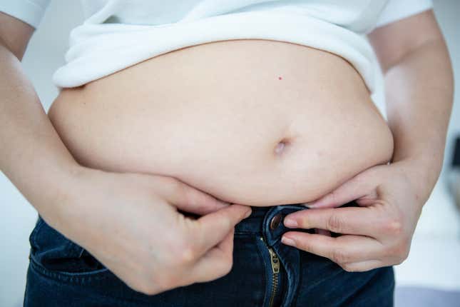 Woman trying to button her pants under her overweight belly