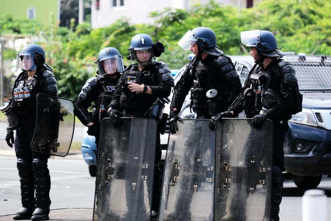 French police stand with their shields at the entrance of the Vallee-du-Tir district, in Noumea on May 14, 2024.