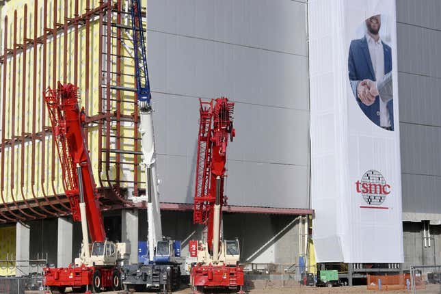 two red trucks with ladders on the corner of a grey building. there's a white banner on the left side of the photo hanging on the building with a man in a suit and a TSMC logo