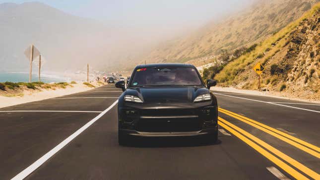 Front view of a camouflaged black Porsche Macan EV driving along the coast