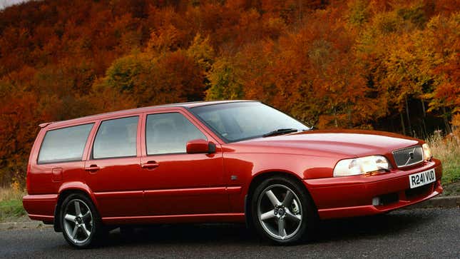 A photo of a red Volvo station wagon with autumn leaves behind it. 