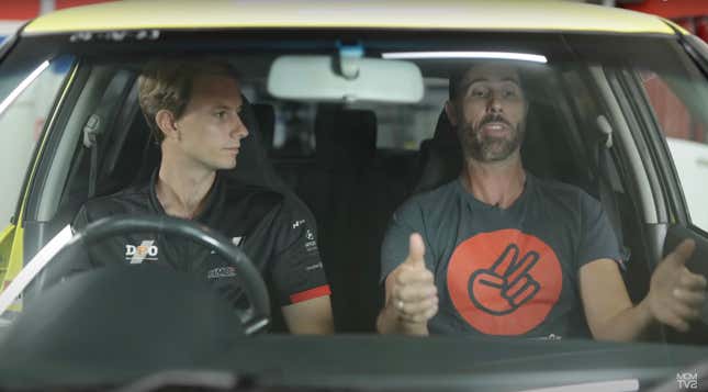 Two Australian men are sitting in a small yellow hatchback. One has his hands out.