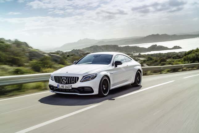 A Mercedes C-Class Coupe driving down a beautiful road with a body of water and mountains in the background