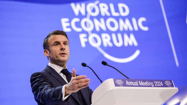 French president Macron speaks at a podium at the World Economic Forum 2024 annual meeting, with one arm outstretched