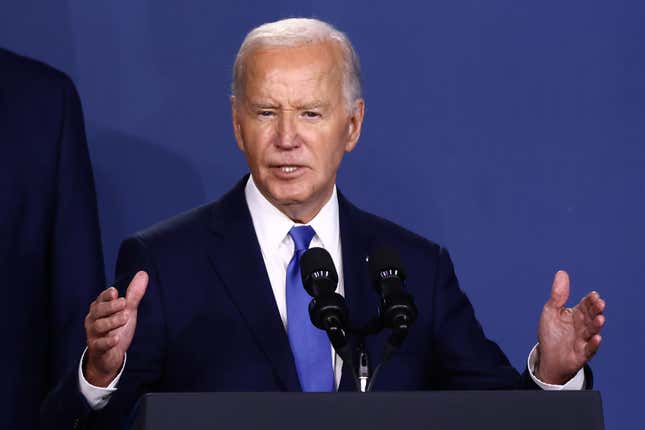 joe biden speaking at a podium wearing a blue tie with both his hands up