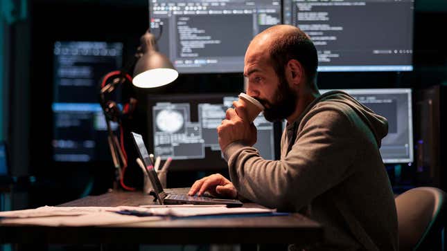 A photo shows a man at a computer drinking coffee in front of monitors. 