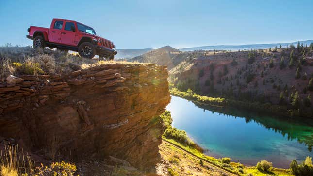 A red Jeep pickup parked on top of a cliff