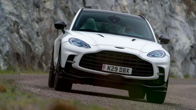 A white 2023 Aston Martin DBX 707 driving on a curvy country road with a rock face in the background.