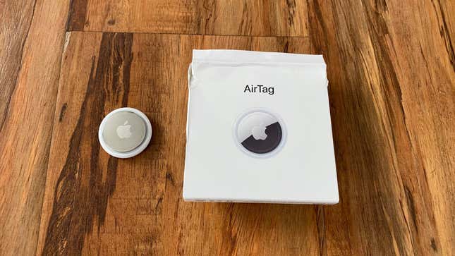 An Apple AirTag on a hardwood floor next to its box