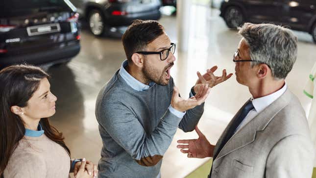 Displeased man and his wife arguing with a salesman in a car showroom.