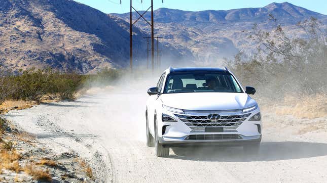 a white Nexo driving down a dirt road in front of mountains and powerlines