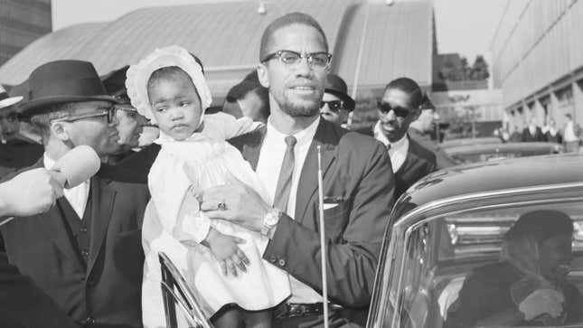 Malcolm X carries his daughter, Ilyasah, as he enters car at John F. Kennedy International Airport.