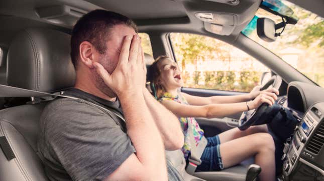 Young kid in drivers' seat manically laughing while father figure in passenger's seat covers his face with his hands