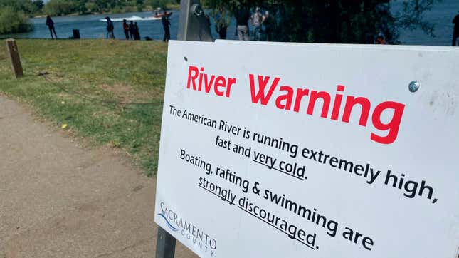 A sign warning the public of dangerous river conditions is posted alongside the American River in Sacramento, California on May 23, 2023.
