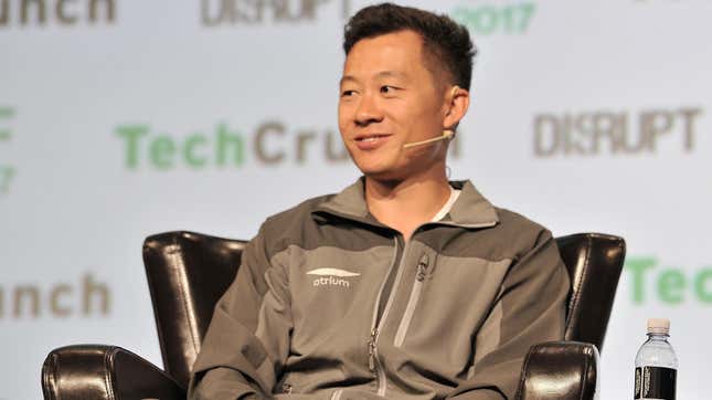 A man sits in a chair on a stage, smiling.